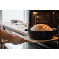 Ein frisches Sauerteigbrot wird in einem gusseisernen Topf aus dem modernen Backofen geholt.